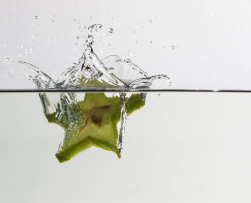 Das querformatige Foto zeigt wie eine Scheibe einer grünen Sternfrucht ins Wasser eintaucht.