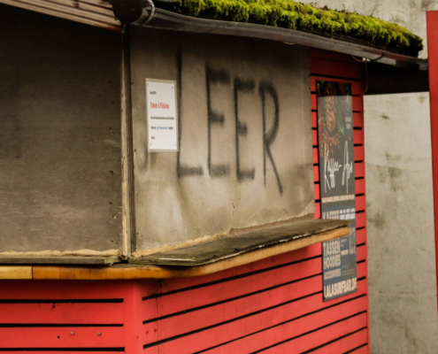 Das querformatige Foto zeigt einen rot angestrichenen Kios mit grünem Grasdach