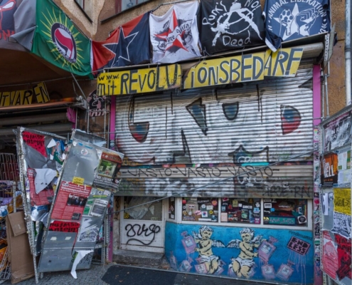 Das querformatige Foto zeigt einen Kiosk mit bemalten, heruntergelassener Jalousie, vielen Tag und Flaggen.