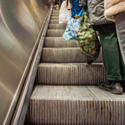 Das querformatige Foto zeigt eine Rolltreppe, auf der Menschen mit vollen Einkaufsbeuteln stehen